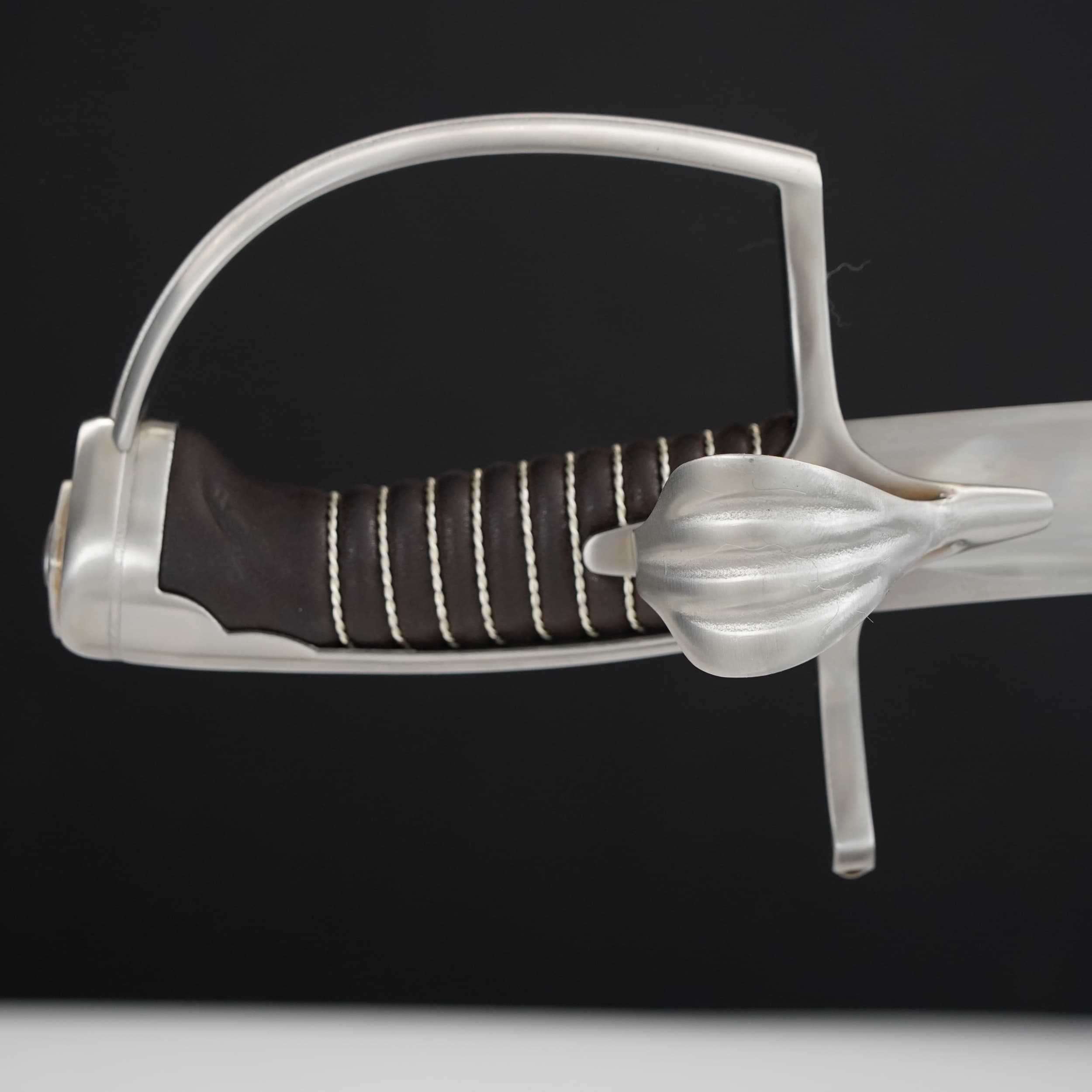 Close-up of a sword with a silver hilt and brown grip on a black background
