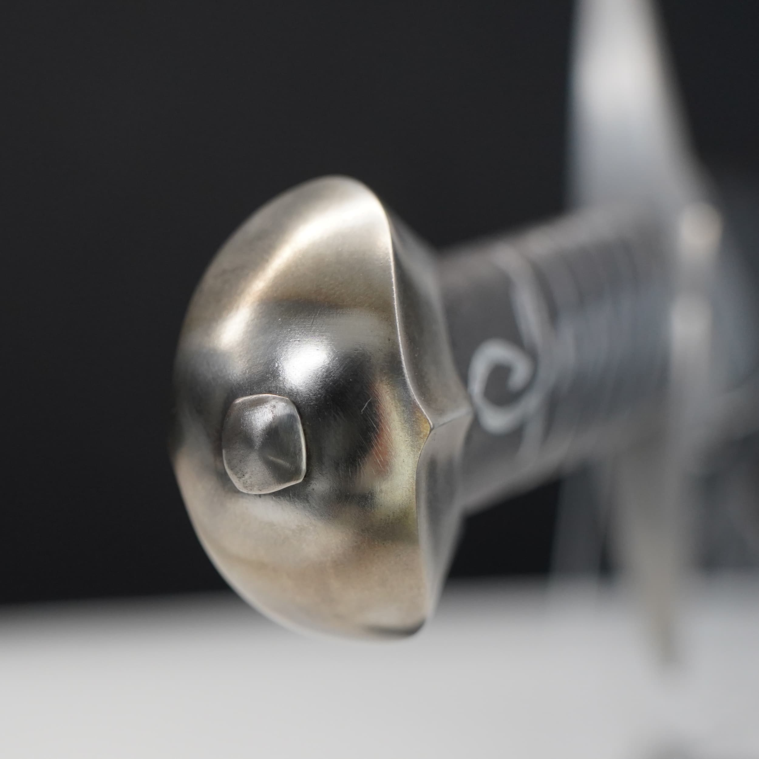 Close-up of a metallic sword hilt with intricate design on a dark background