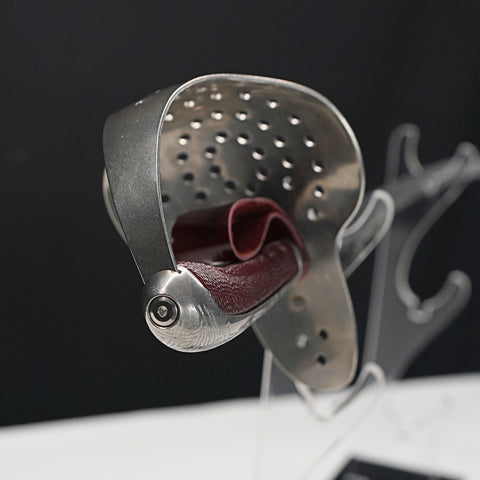 Metallic shoe shine tool with red interior on a stand against a dark background