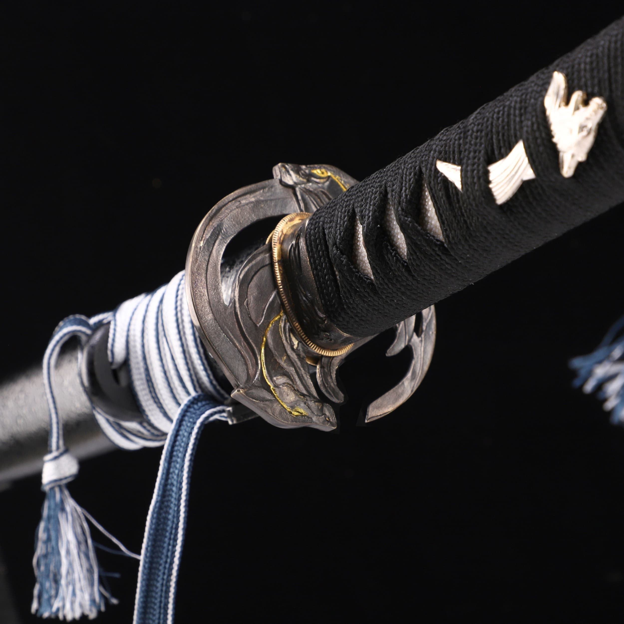 Close-up of a Japanese sword with black sheath and decorative elements on a black background
